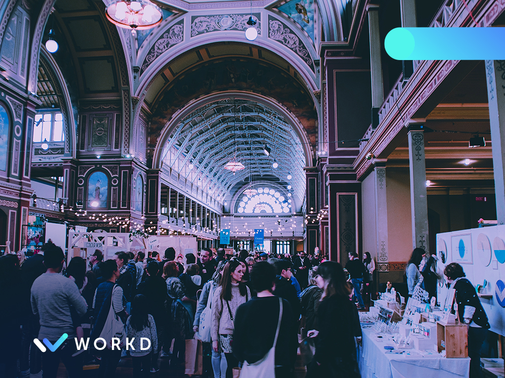 Large crowd of people gathered in a conference hall with various exhibitors.